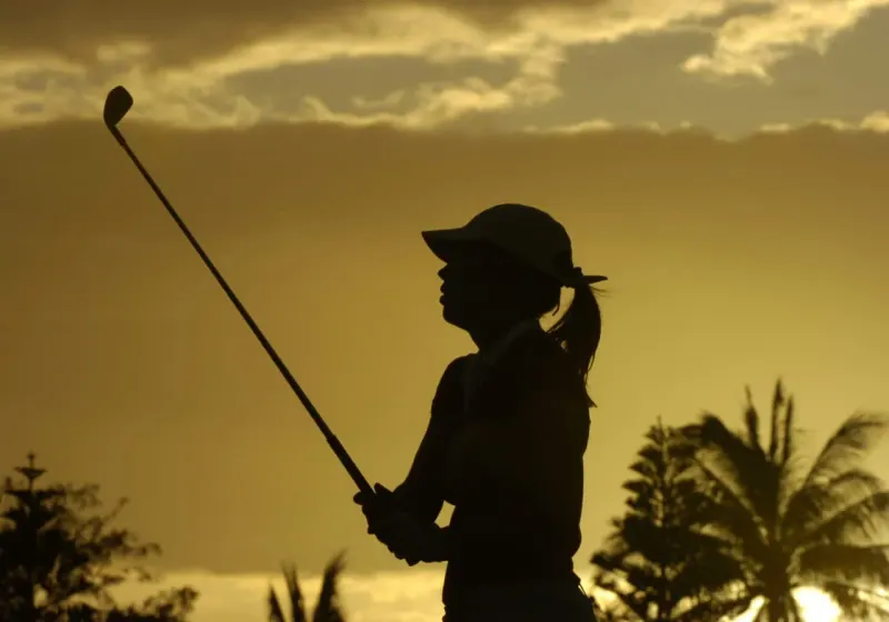 A mostly coral golf ball fractures as a club knocks away a segment, symbolizing golf’s risk of alienating women.