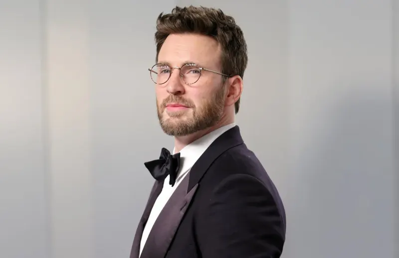 A shield-shaped mansion tips toward the East Coast as coins fall away, symbolizing Chris Evans’s discounted home sale.