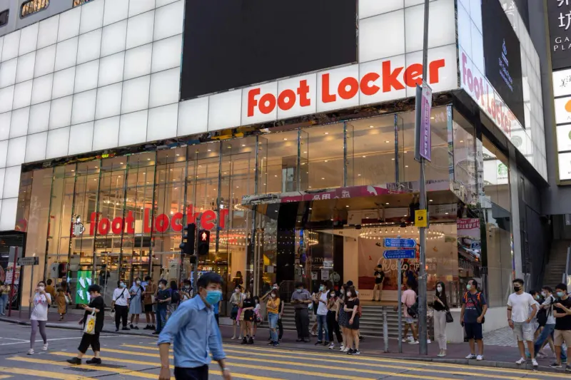 A golden sneaker sinks into a clearance bin, symbolizing Foot Locker’s difficult turnaround.