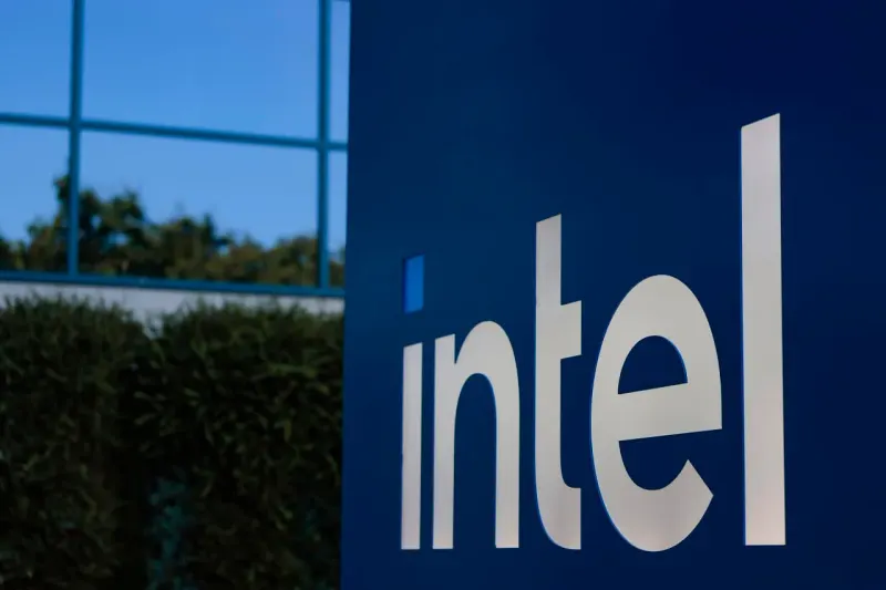 A laptop squeezed between memory chips and shrinking coins symbolizes pressure on Intel’s PC business.