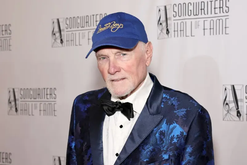 A jewel-like mansion protected by pine branches and blue water symbolizes conservation around Mike Love’s estate.