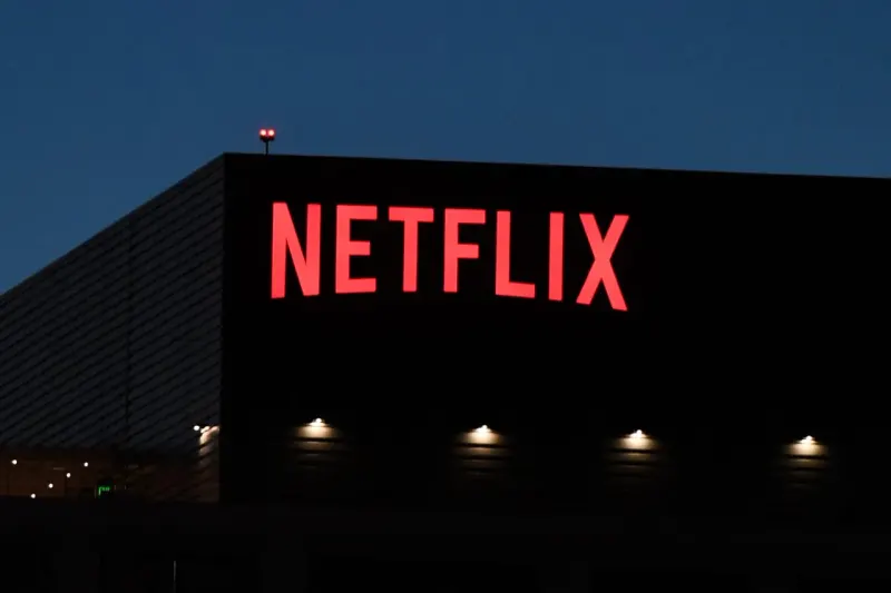 A red film strip climbs against converging dark streams, symbolizing Netflix’s viewership and competition challenges.