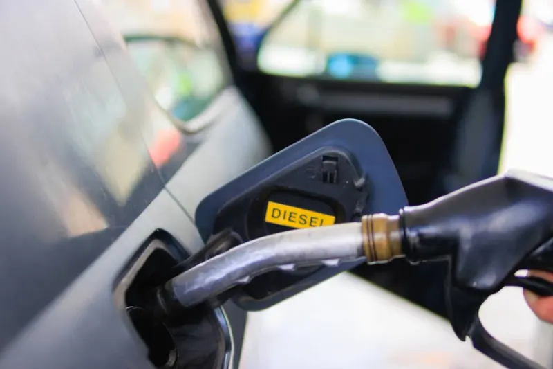 A diesel nozzle becomes a rising thermometer, symbolizing fuel-driven inflation.