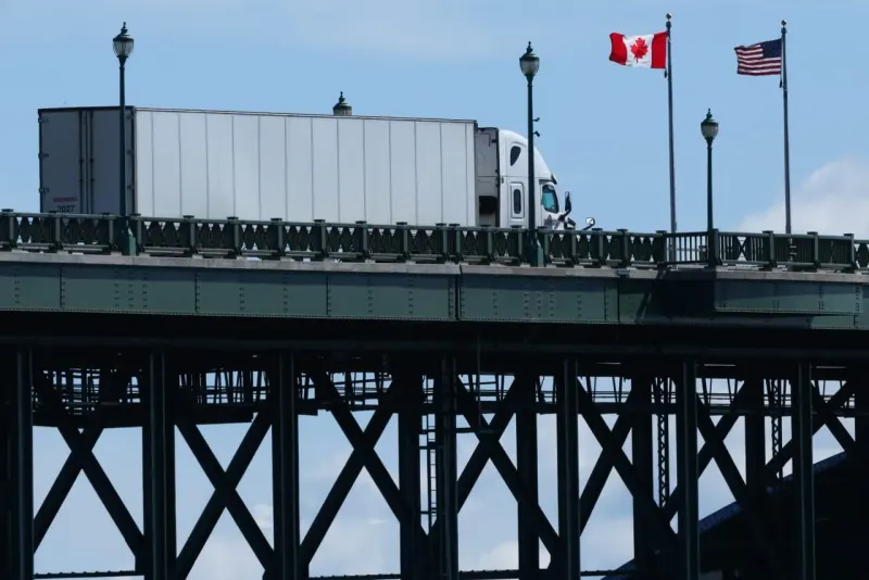 A nearly completed puzzle bridge spans tariff barriers, symbolizing unfinished U.S.-Canada trade talks.